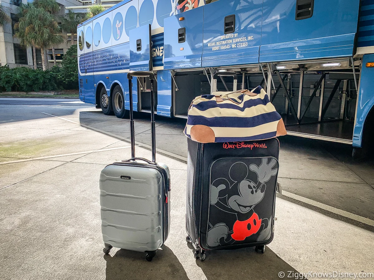 Two luggage bags, one of it having a Disney theme showing Mickey Mouse and behind it is a bluish Disney themed bus with its compartment open.