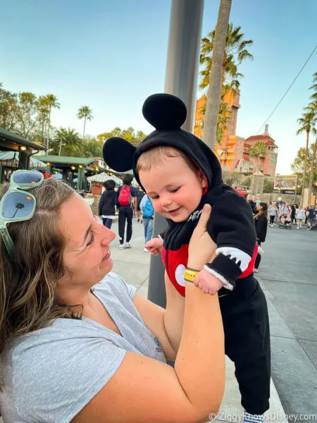holding up baby in Mickey Mouse outfit in front of Tower of Terror